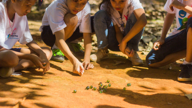 Matéria Prima Crianças brincando com bolinhas de gude na oficina de Jogos e Brincadeiras